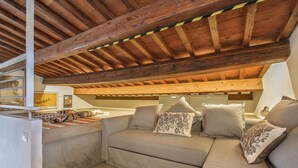 A cozy loft-style room with a wooden ceiling, a sofa with patterned cushions, and a small table with decorative items. - Maggio In Florence (Firenze)