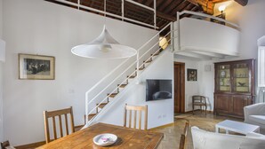 A spacious living area with a wooden dining table, a white sofa, a wooden staircase, and a TV mounted on the wall. - Maggio In Florence (Firenze)