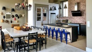 Una cocina moderna con pared de ladrillo, una zona de comedor con taburetes azules y una araña.