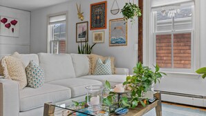 Un salon avec un canapé blanc, une table basse en bois et divers éléments de décoration murale, notamment des tableaux encadrés et une plante.