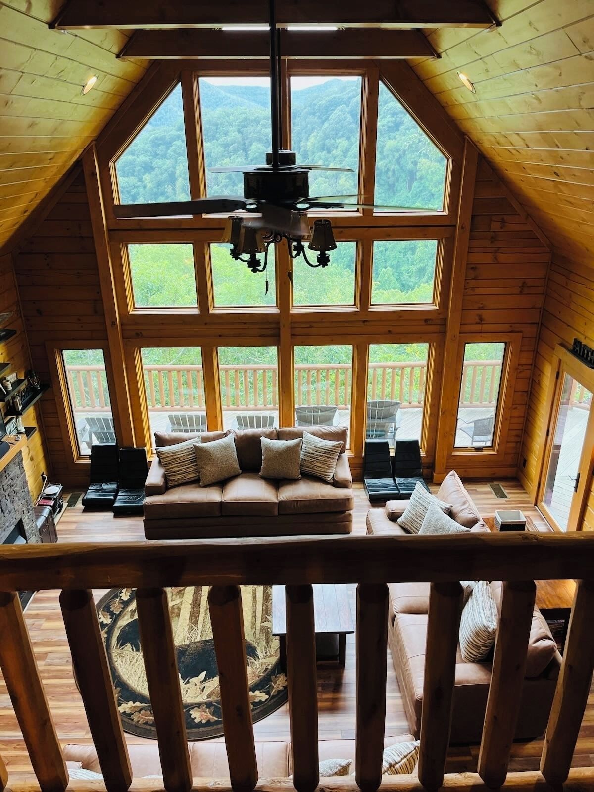A cozy cabin with a loft bedroom featuring a large window, a wooden ceiling, and a central chandelier.