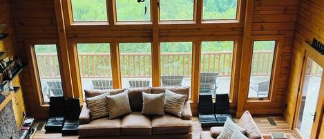 A cozy cabin with a loft bedroom featuring a large window, a wooden ceiling, and a central chandelier.