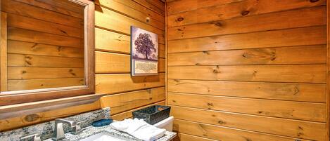 A wooden cabin bathroom with a granite countertop sink, a mirror, and a framed picture of a tree.