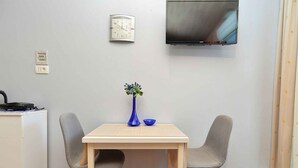 A small dining area with a table and two chairs, a vase with flowers, a bowl, and a television mounted on the wall. - Holiday apartment with air conditioning (Fažana)