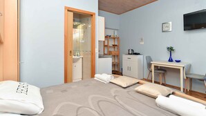 A bedroom with a bed, a desk, a chair, a TV, and a bathroom visible through an open door. - Holiday apartment with air conditioning (Fažana)