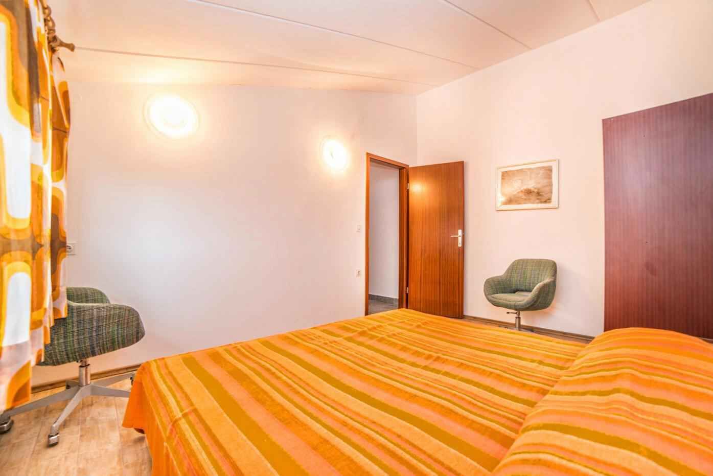 A bedroom with a bed, a chair, a door, and a wall-mounted picture.