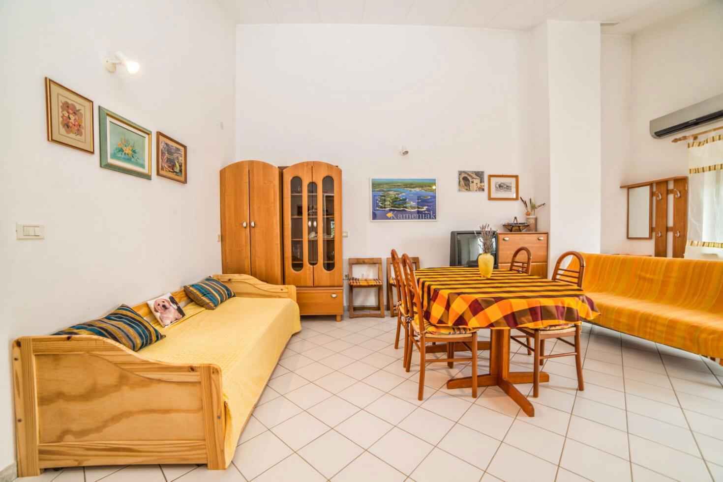 A cozy living room with a sofa, a dining table with chairs, a wooden cabinet, and a TV.