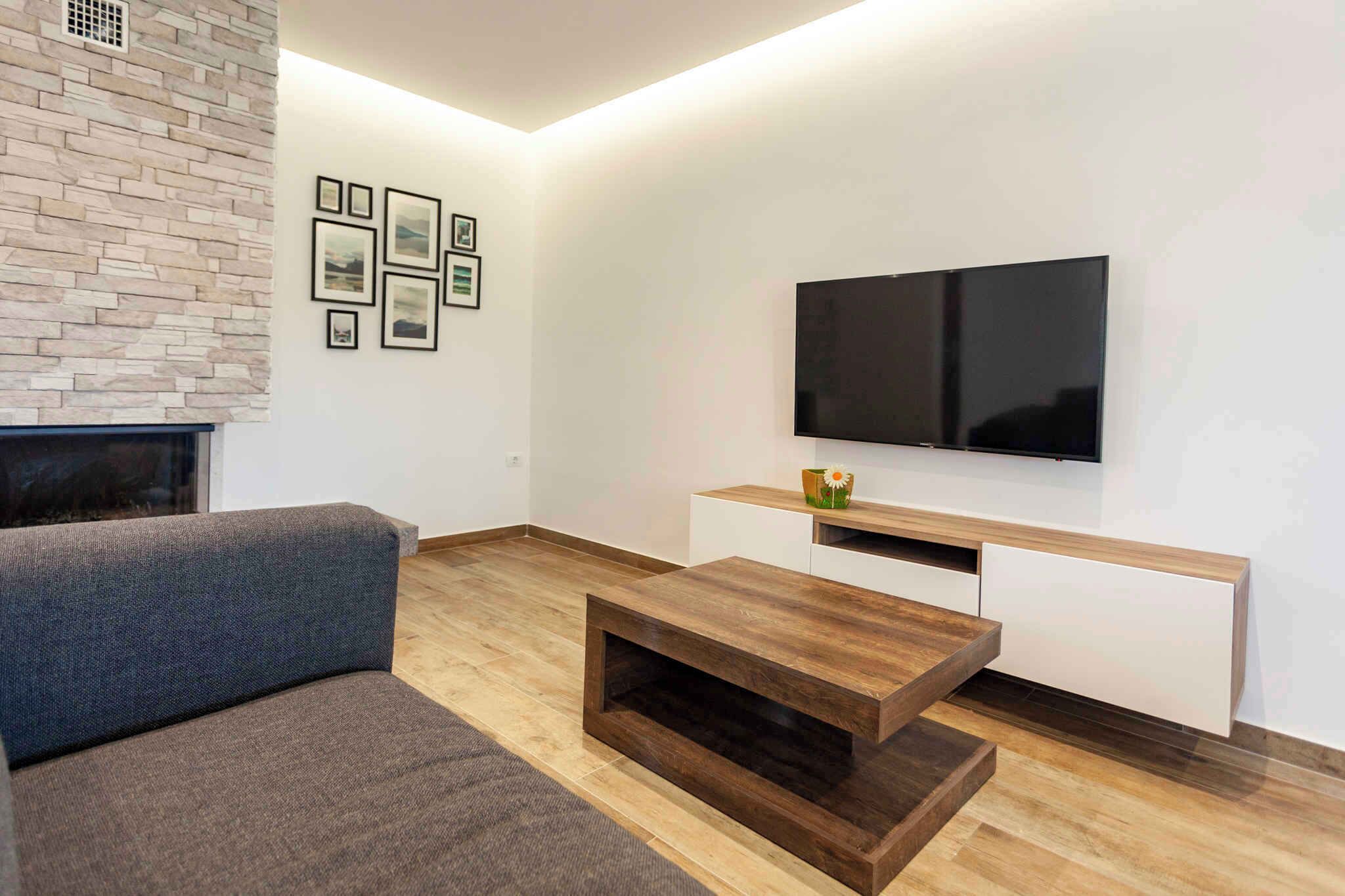 Una sala de estar moderna con una chimenea de piedra, un televisor de pantalla plana sobre un mueble blanco y un sofá gris.