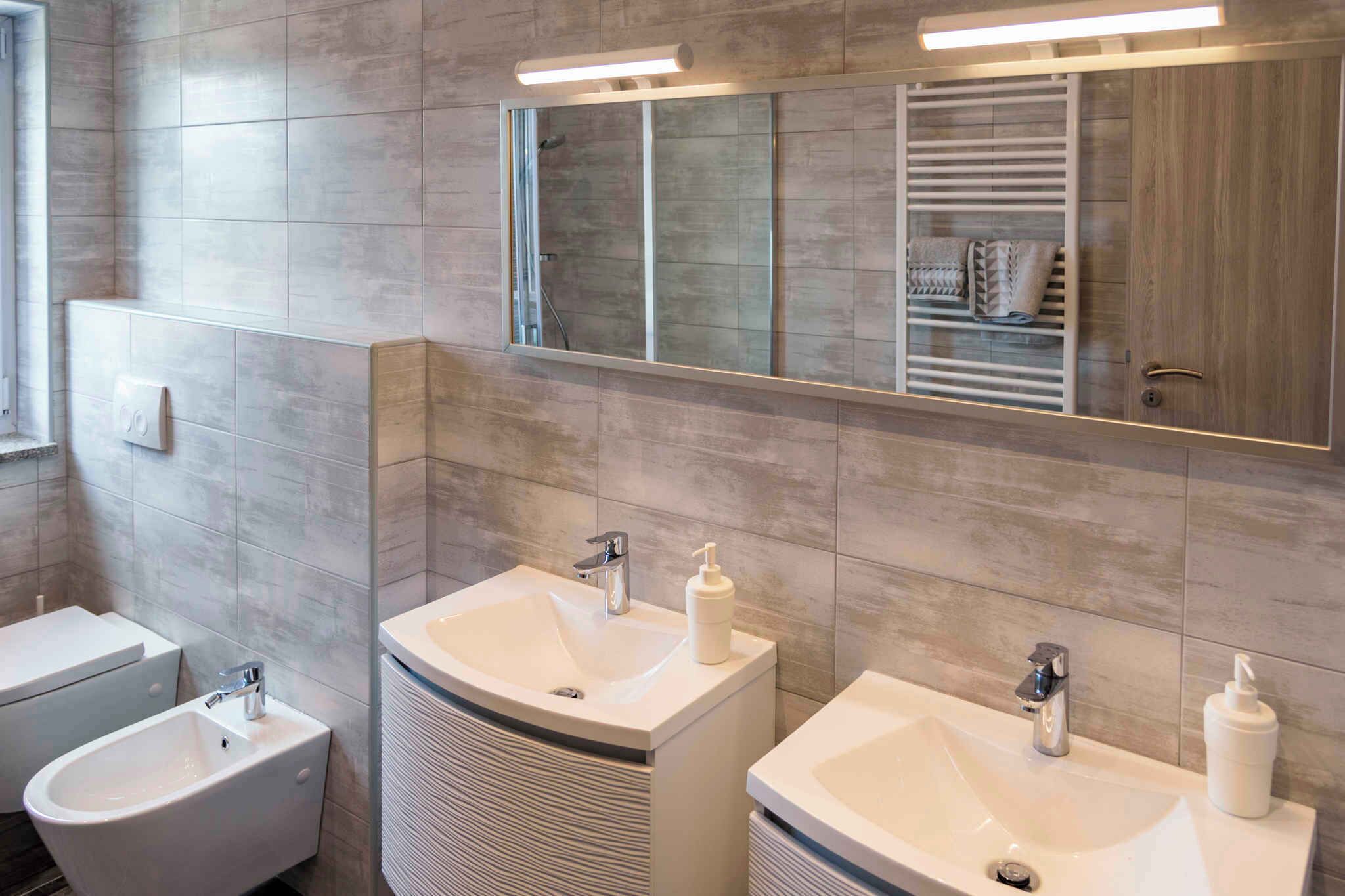 Ein modernes Badezimmer mit zwei Waschbecken, einem Bidet und einem großen Spiegel.