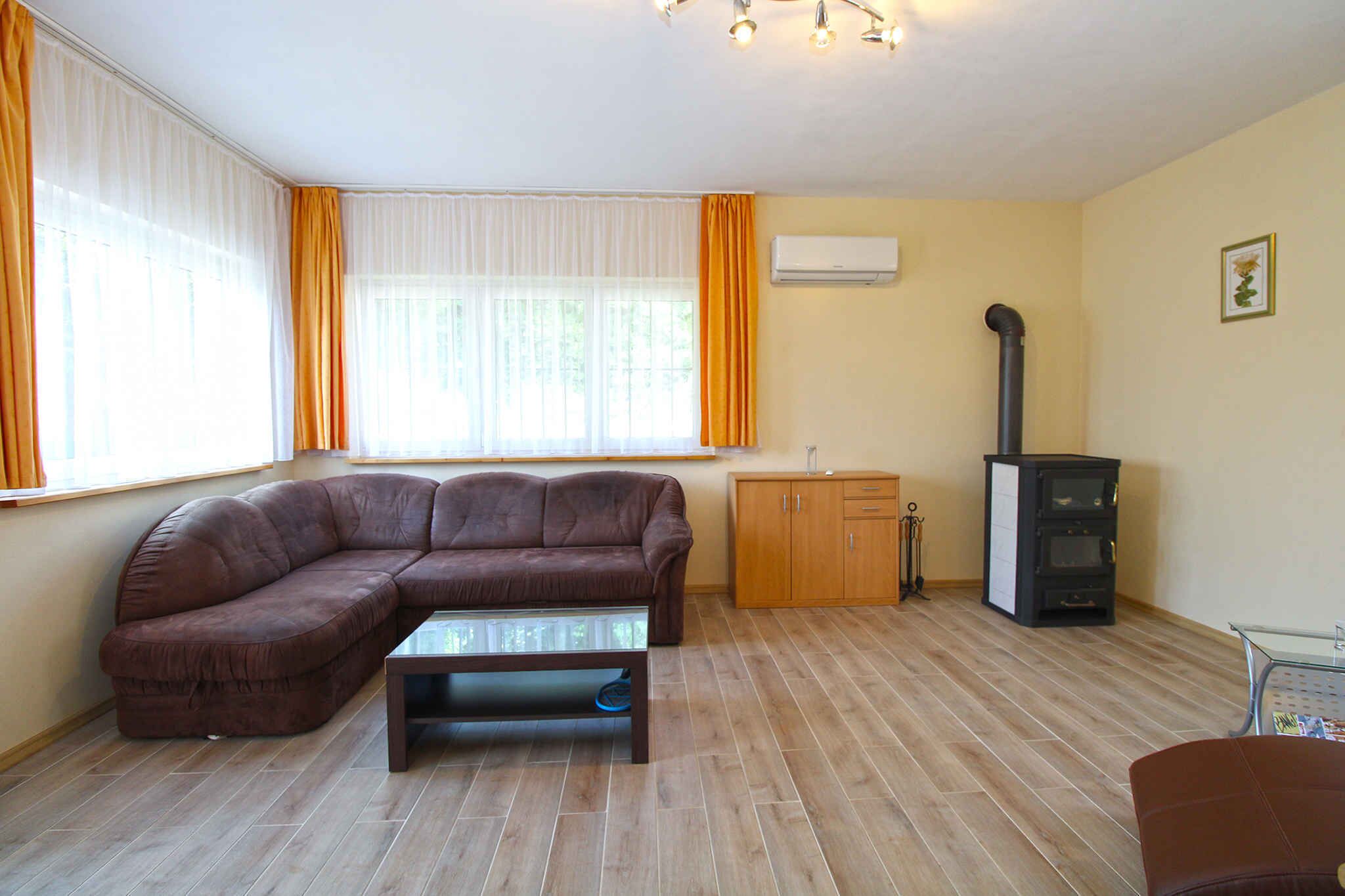 Ein Wohnzimmer mit einem braunen Ecksofa, einem Glastisch, einem Holzschrank und einem schwarzen Kaminofen.