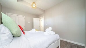 A hotel room with a bed, pillows, a red object on the bed, and a white door in the background. - BoHo Chic Suite - Long Stays - Fireplace - Garage
 (Edmonton)