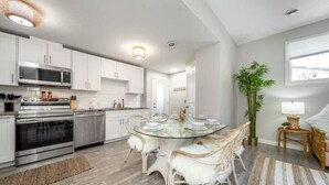 A modern kitchen with white cabinets, stainless steel appliances, and a glass dining table with white chairs. - BoHo Chic Suite - Long Stays - Fireplace - Garage
 (Edmonton)