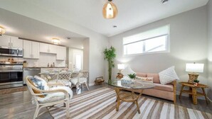 A modern kitchen with white cabinets, a dining area with wicker chairs, a glass coffee table, and a cozy seating area with a sofa and side tables. - BoHo Chic Suite - Long Stays - Fireplace - Garage
 (Edmonton)