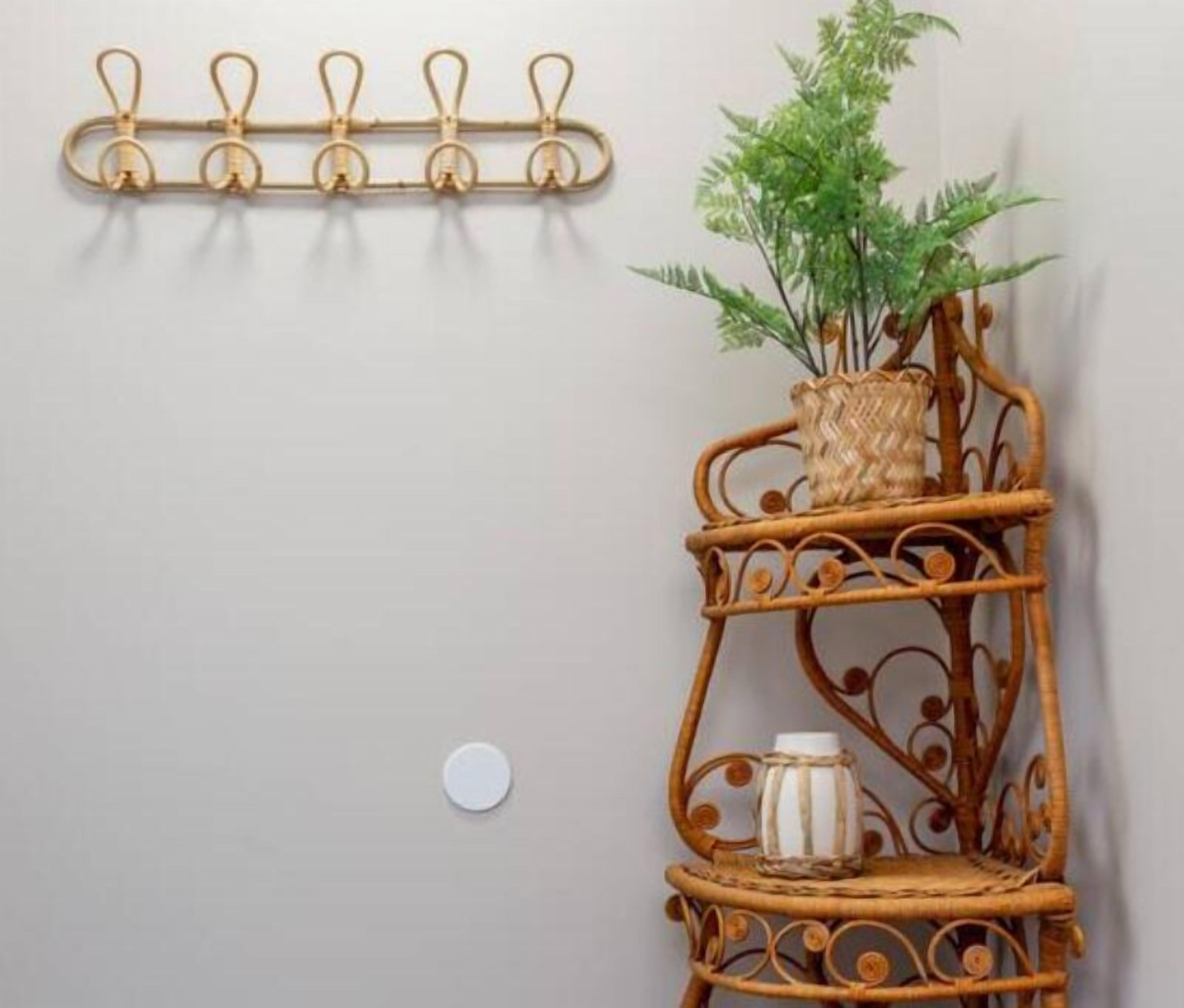 Un perchero metálico sujeto a la pared, con ganchos y un estante de mimbre que tiene una planta y un recipiente blanco.