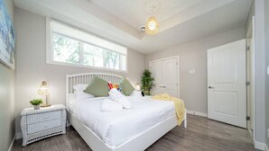A bedroom with a large bed, a nightstand with a lamp, a window, and a door. - BoHo Chic Suite - Long Stays - Fireplace - Garage
 (Edmonton)