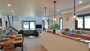 A modern kitchen with a central island, a dining area with a table and chairs, a living room with a sofa, a staircase, and a large window providing natural light. - Stunning home in Maillane with WiFi (Maillane)