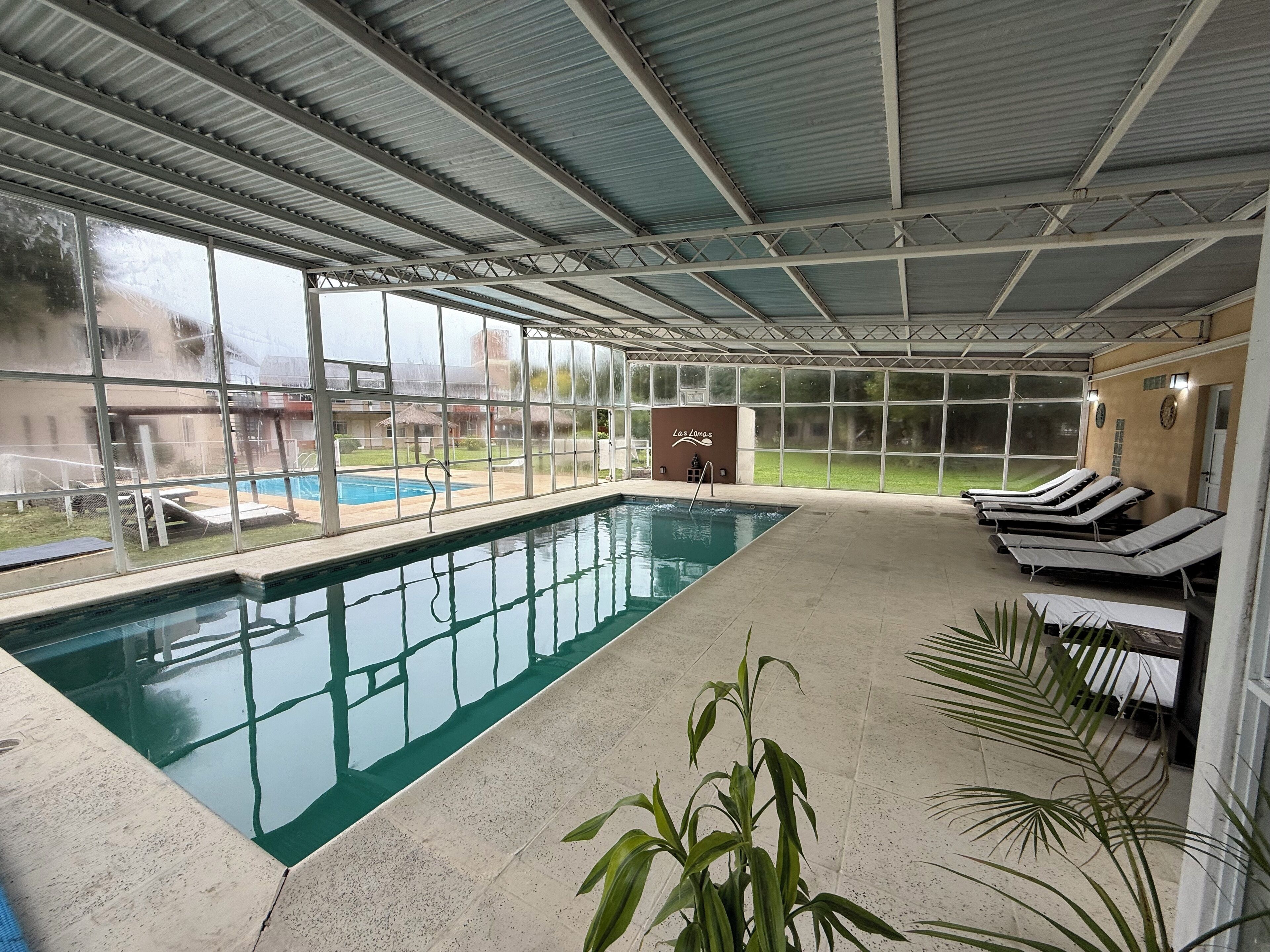 An indoor swimming pool with clear glass walls, lounge chairs, and a sign reading "Las Lomas."