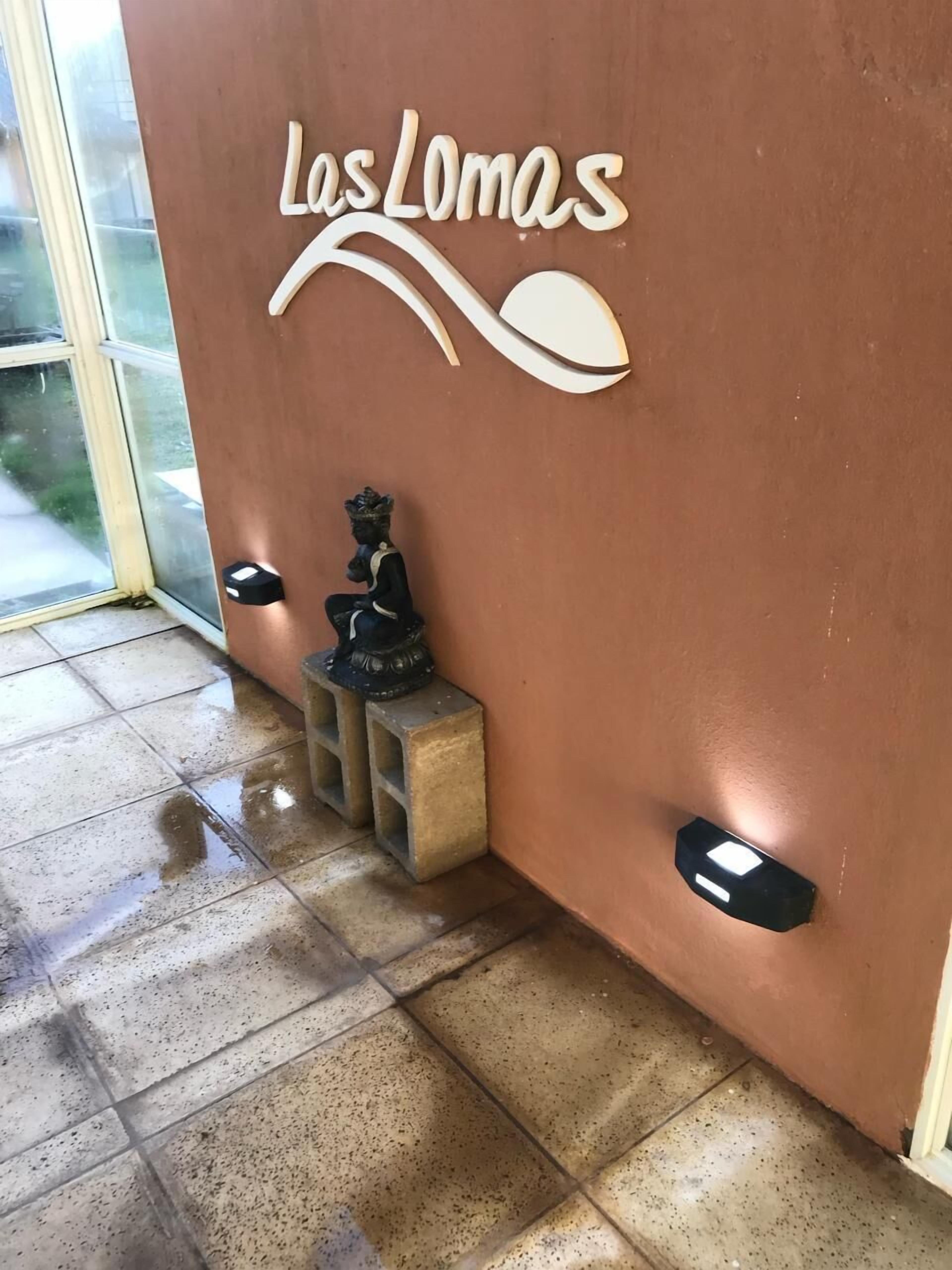 Un'area reception con un cartello che riporta "Las Lomas", una piccola statua di Buddha e un pavimento piastrellato.