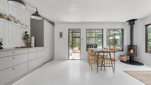 A modern kitchen with white cabinetry, a dining area with wooden chairs, and a wood-burning stove.