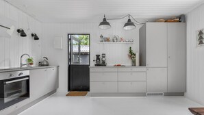 A modern kitchen with white cabinetry, a built-in oven, a coffee maker, and pendant lights.