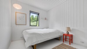 A minimalist bedroom with a bed, a window, a lamp, and a rug.
