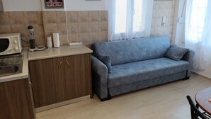 A kitchenette with a microwave, toaster, and coffee maker, a grey sofa, and a dining table with chairs. - Studio 'Gorgona' with sea view, Wi-Fi and air conditioning (Loutra)