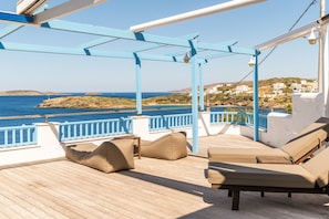 A deck with lounge chairs and a view of the sea and buildings. - Villa "Blue Waves View Andros" with Sea View, Private Pool & Wi-Fi (Andros)