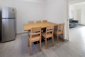 Une cuisine moderne avec un réfrigérateur en acier inoxydable, une table à manger en bois avec six chaises, et un canapé gris en arrière-plan.