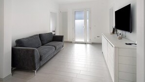 Un salon moderne avec un canapé gris, un téléviseur à écran plat fixé au mur et un meuble blanc.