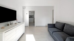 Un salon moderne avec un téléviseur à écran plat, un canapé gris et un meuble de rangement blanc.