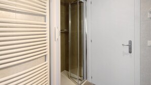 Une salle de bain avec une douche à parois de verre, une porte blanche et un sol carrelé.