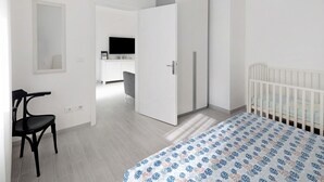 Une chambre à coucher avec un lit, un berceau, une chaise, une armoire et un téléviseur à l’arrière-plan.