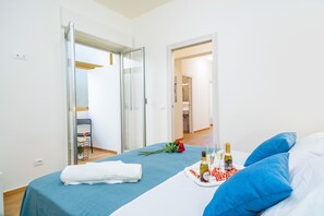 Une chambre d’hôtel avec un lit, un plateau avec une bouteille et des verres, un bouquet de fleurs et une serviette.