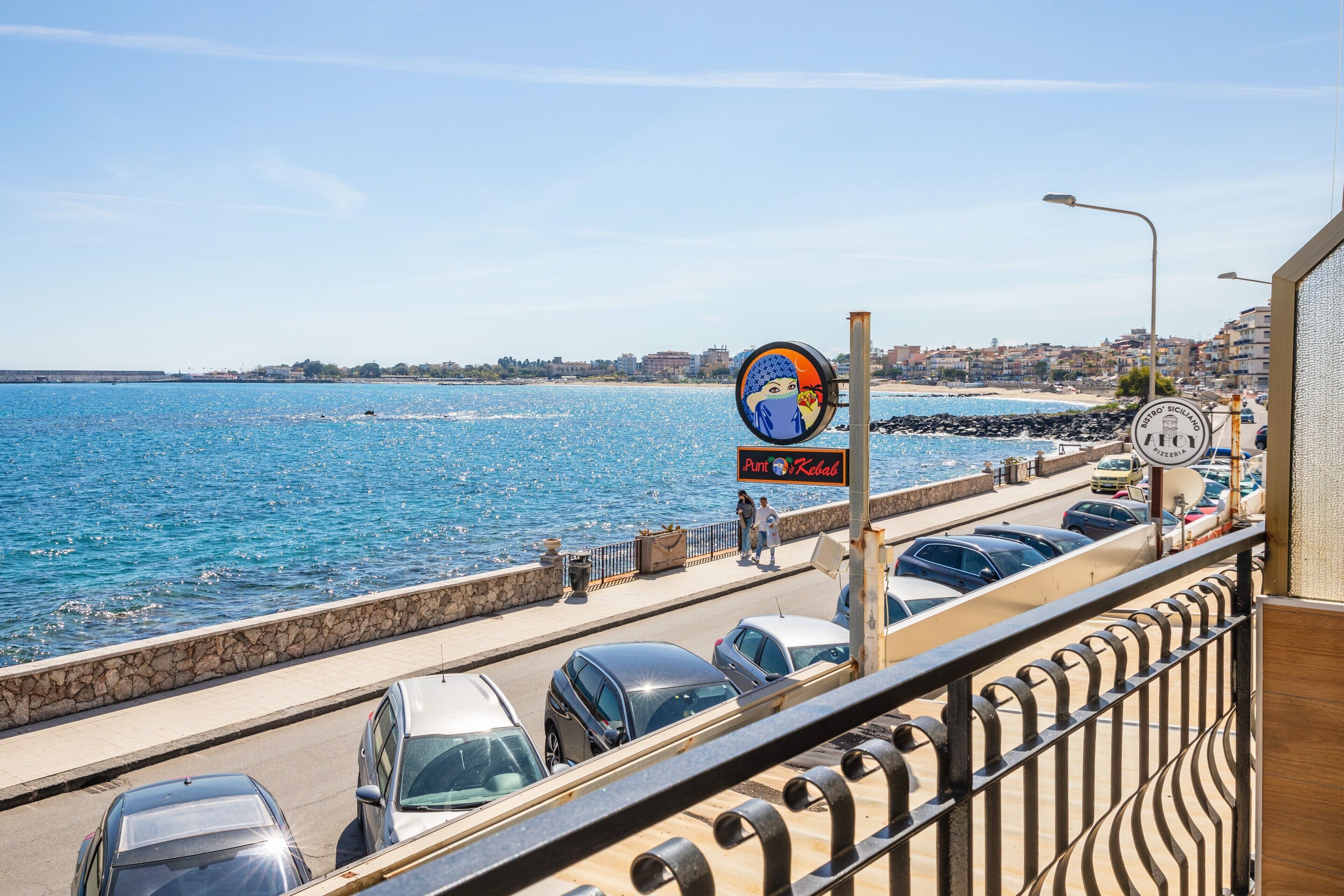 Une route côtière bordée de voitures garées, un chemin piétonnier et une vue sur la mer.