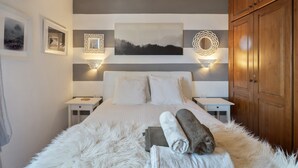 Camera da letto con un letto, pareti bianche, un quadro, due comodini e un armadio in legno.