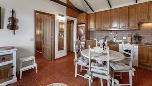 Una cucina con mobili in legno, un tavolo da pranzo con sedie, un violino appeso al muro e un piccolo sgabello.