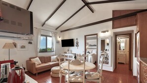 Un'ampia zona giorno con divano, tavolo da pranzo e sedie, una cucina sullo sfondo e una TV fissata al muro.