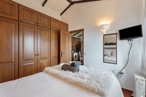 Un dormitorio con cama, armario de madera, televisor empotrado en la pared y radiador.