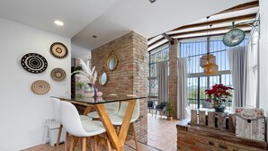 Un coin repas avec une table en verre, des chaises blanches et un mur en briques.