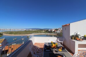A balcony with a table set for breakfast, overlooking a coastal area with boats and a beach.
