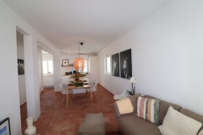 A modern living room with a sofa, a dining area with chairs, and a kitchen in the background.