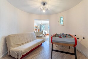 A room with a sofa, a foosball table, and a dining area in the background.