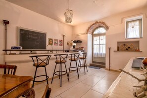Una cocina con una pizarra, taburetes de bar, una mesa de madera y un colgador con luz.