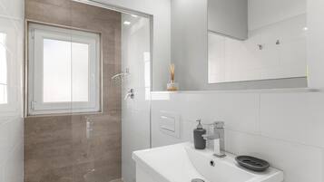 Un baño moderno con cabina de ducha de vidrio, un lavabo blanco y un espejo encima.