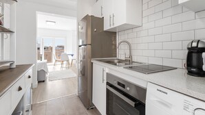Une cuisine moderne avec des meubles blancs, un réfrigérateur en acier inoxydable, un lave-vaisselle et une machine à café.