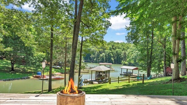 A wooden deck with a fire pit, overlooking a lake with docks and a gazebo.