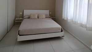 Een slaapkamer met een bed, nachtkastjes, een garderobe en een raam met gordijnen.