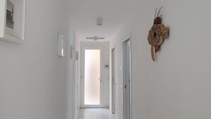 Een hal met witte wanden, een betegelde vloer, een deur aan het einde en een decoratief object aan de muur.