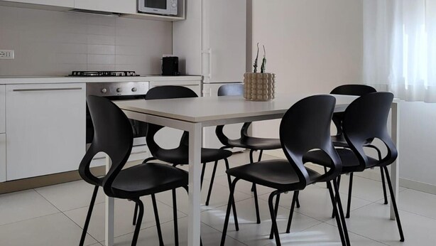 Een moderne keuken met witte kastjes, een magnetron, een fornuis en een eettafel met zwarte stoelen.