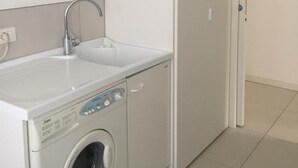 Een kleine wasruimte met een wasmachine, een spoelbak en een deur naar een andere kamer.